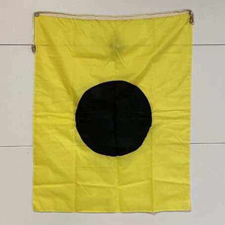 Authentic Nautical Lima Flag - Signal L Yellow signal flag with black circle displayed against a wall, slight fabric creases visible.
