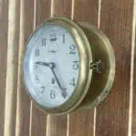 Mounted vintage brass nautical clock with latch visible on right side.
