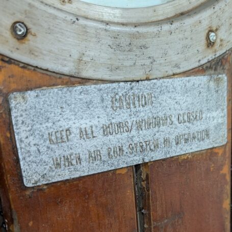 Close-up of an engraved metal plate on a salvaged ship's door, showing patina and maritime wear.