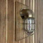 the Vintage Brass Nautical Wall-Mounted Light On Wood Base on a wall