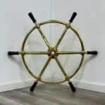 Front view of vintage-style brass ship's wheel with black wooden handles