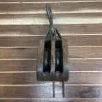 Nautical double pulley resting on wooden surface with iron hook extended