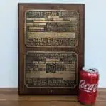 Front view of General Electric brass plates mounted on wood, with a soda can for size reference