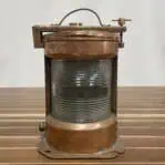Front view of vintage copper starboard navigation light with Fresnel lens and dented base.