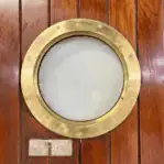 Rear close-up of brass ship porthole window in wood door
