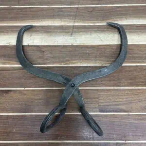 Overhead view of vintage iron ice tongs showing curved gripping arms and rusted surface.