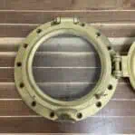 Iron ship porthole opened on wood surface with visible mounting holes