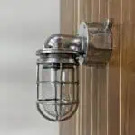 Polished aluminum nautical wall light mounted on wood panel