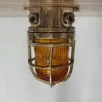 Mounted brass ceiling fixture with protective cage and orange lens