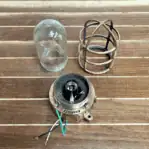 Disassembled brass light with housing, glass globe, and tall protective cage