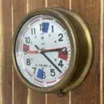 Side view of vintage Polaris brass ship clock mounted on wood paneling