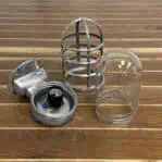 Disassembled vintage aluminum nautical bulkhead light showing cage, glass, and socket