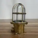 Salvaged brass ceiling light with glass globe and cage - resting on wood surface