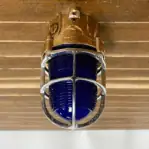 Brass ceiling light with blue Fresnel glass and protective cage