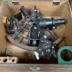 nautical sextant top view resting inside fitted wooden storage box